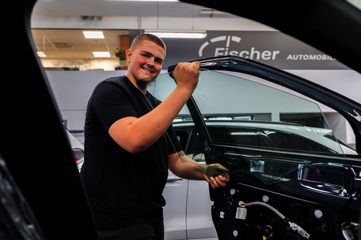 Junger Mechaniker setzt eine Scheibe in eine Autotür ein.